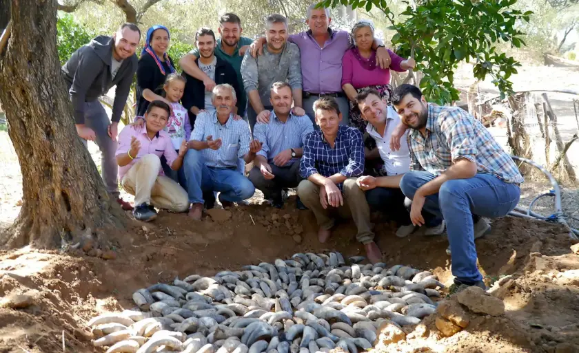Groupe de personnes posant autour d'un tas de bananes de terre dans un cadre rural.