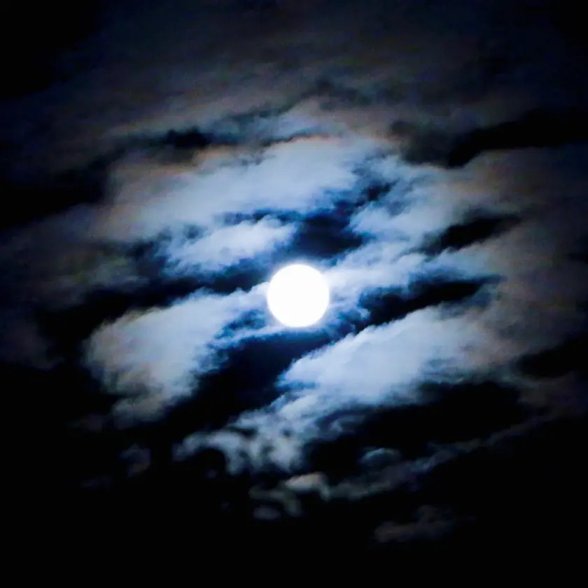 Lune brillante émergeant à travers des nuages sombres dans un ciel nocturne.