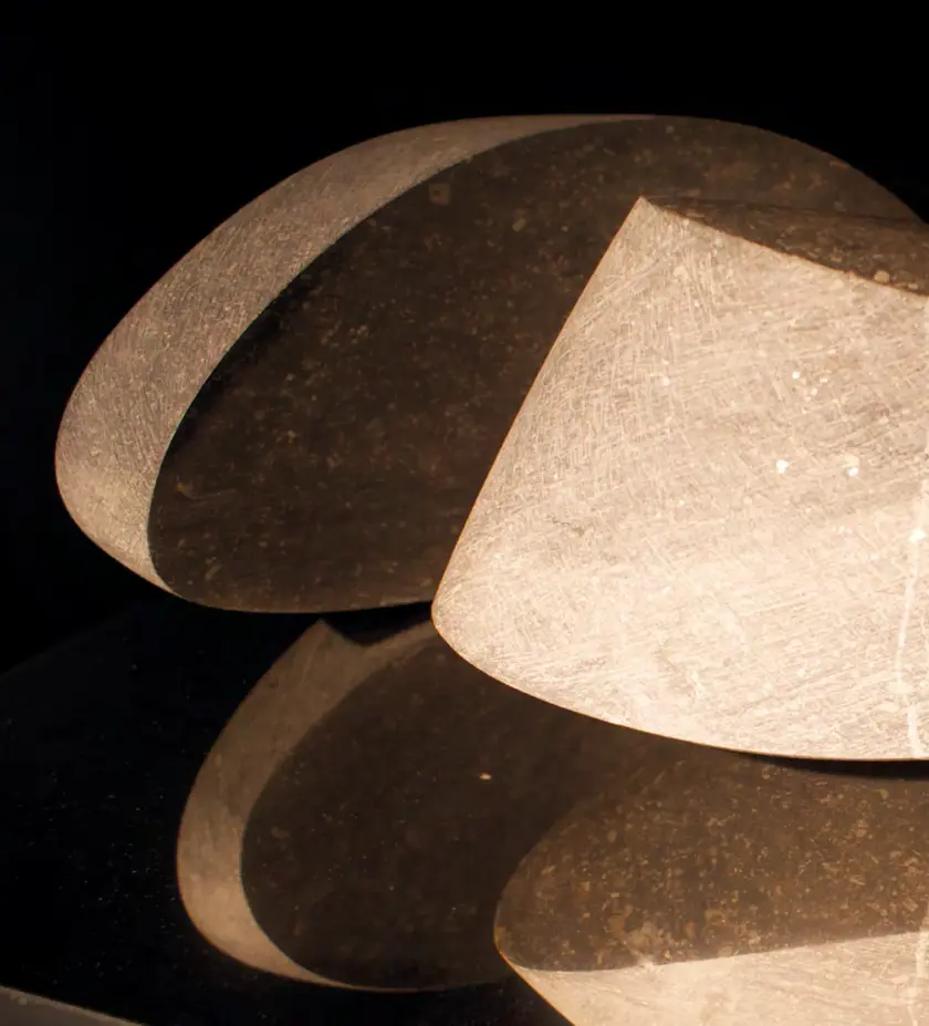 Deux formes géométriques en pierre translucide, éclairées, avec un reflet sur une surface noire.