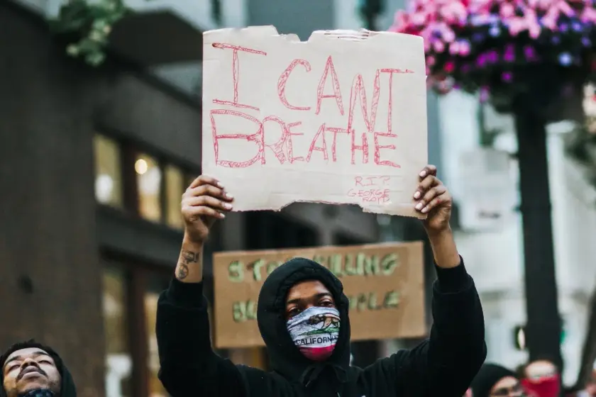 Manifestant portant un panneau avec l'inscription 'I CAN'T BREATHE', entouré d'autres manifestants.