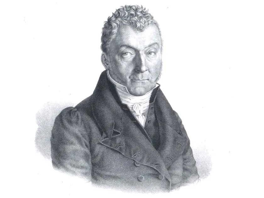 Portrait en noir et blanc d'un homme au visage sérieux, portant un manteau et une chemise à col.