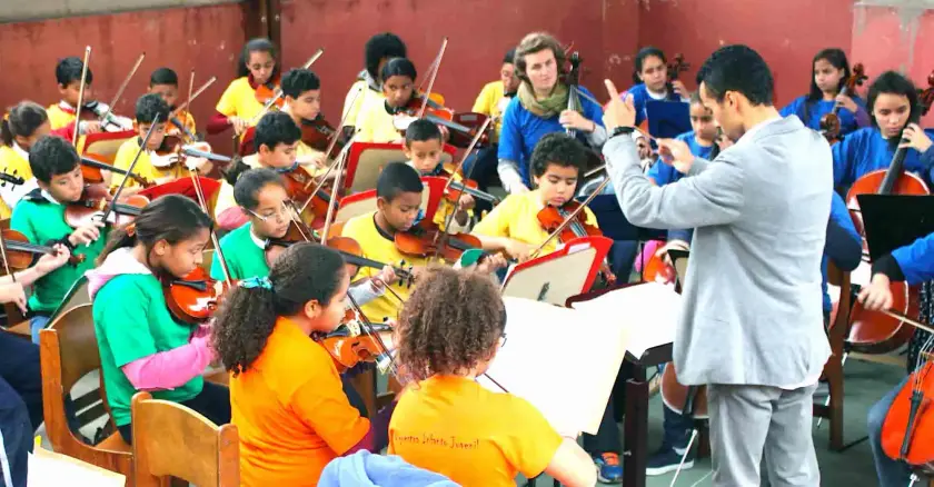 Un orchestre d'enfants en répétition, dirigé par un chef d'orchestre, dans une salle de musique.