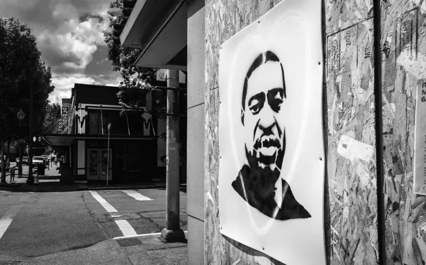 Portrait en noir et blanc de George Floyd affiché sur un mur en bois, avec une rue en arrière-plan.