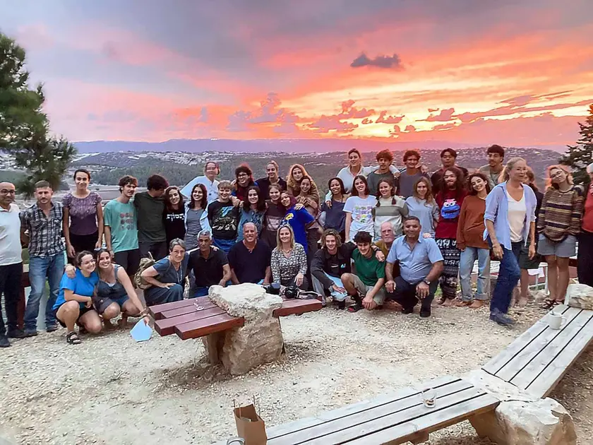 Groupe de personnes posant ensemble au coucher de soleil, avec des collines en arrière-plan.