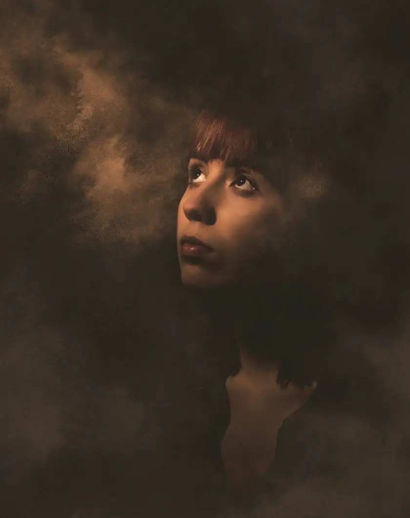 Portrait d'une femme avec des cheveux roux, regardant vers le haut dans une ambiance sombre et brumeuse.