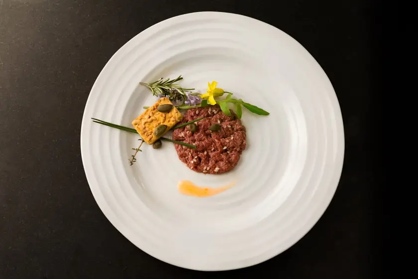 Assiette blanche contenant un tartare de viande, décoré de fleurs comestibles et d'herbes.