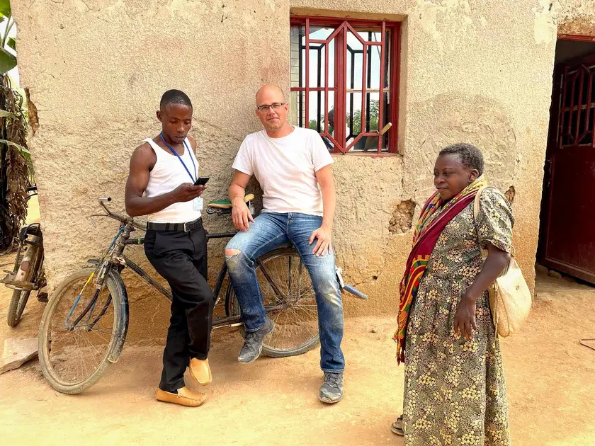 Trois personnes se tiennent devant un mur en béton, l'une sur un vélo, les autres discutant.