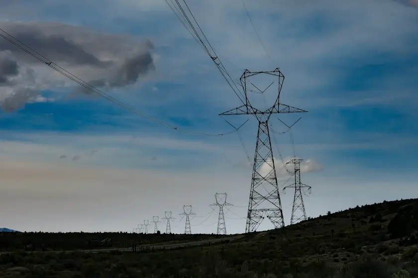 Lignes électriques et pylônes sur un paysage vallonné sous un ciel nuageux.