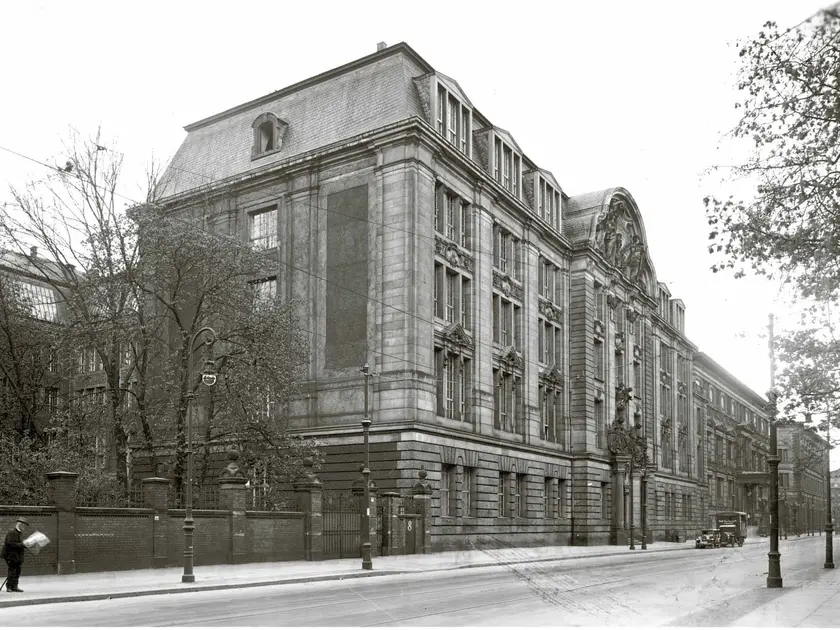 Bâtiment historique en pierre avec une architecture élaborée, entouré d'arbres et de rues pavées.