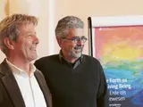 Deux hommes souriants se tenant côte à côte devant un panneau coloré.