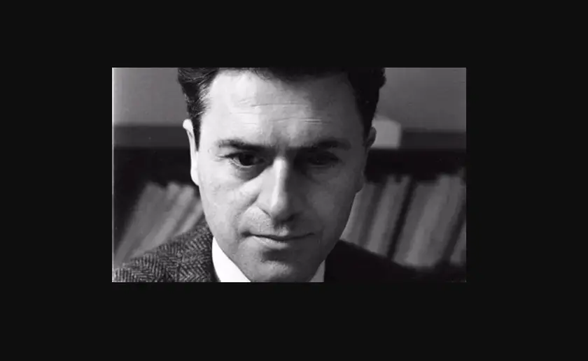 Portrait en noir et blanc d'un homme pensif, avec des livres flous en arrière-plan.