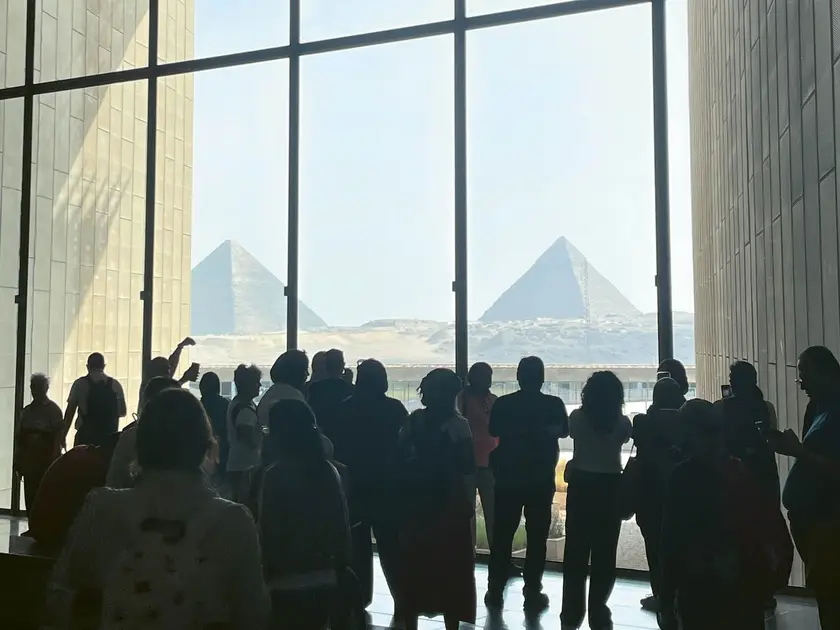 Silhouettes de visiteurs observant les pyramides à travers de grandes fenêtres.