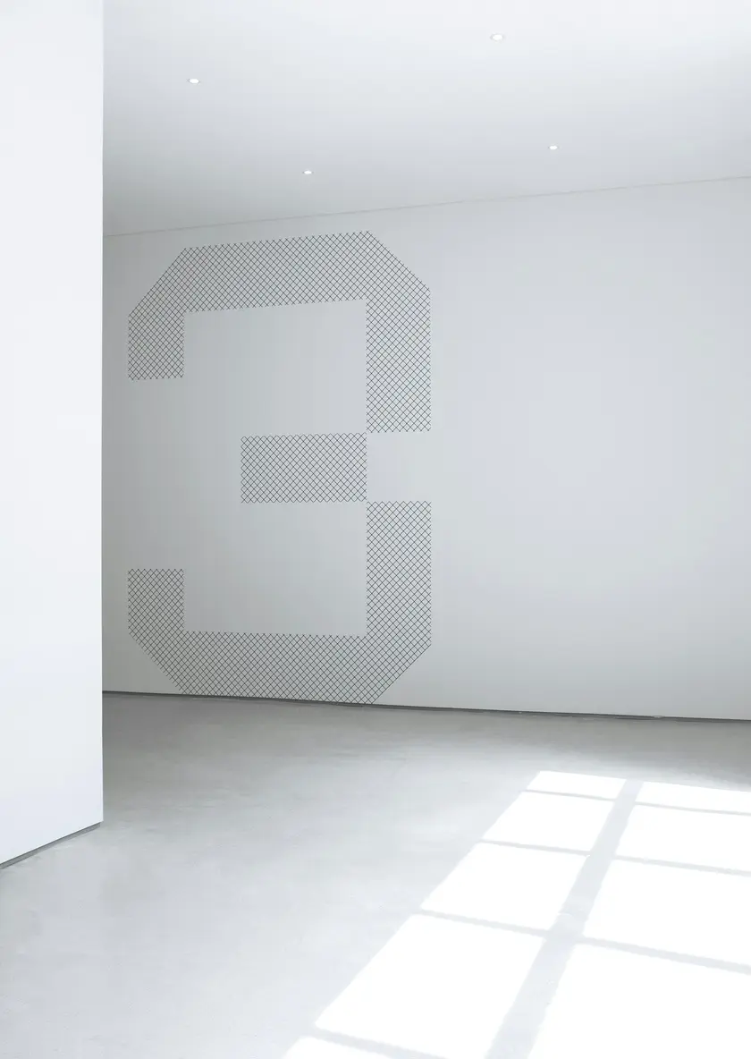 Un intérieur minimaliste avec un mur blanc portant un grand chiffre trois en motif perforé.