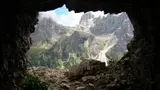 Vue d'une montagne à travers l'ouverture d'une grotte, avec des nuages et des rochers.