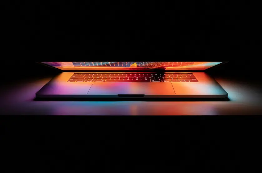 Un ordinateur portable ouvert émettant des lumières colorées sur un fond sombre.
