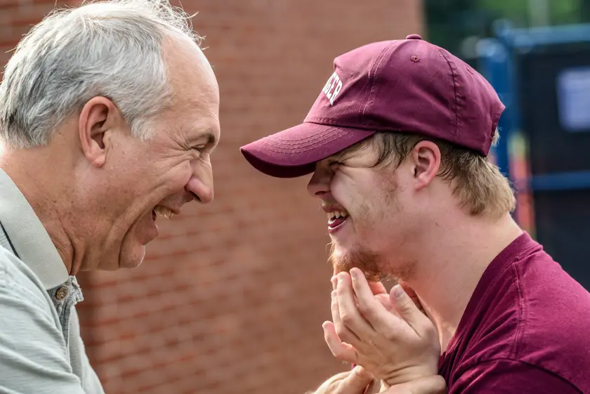 Deux hommes souriants se regardent avec complicité, l'un portant une casquette maroon.