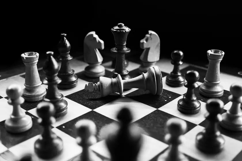 Échiquier en noir et blanc avec des pièces de jeu, dont un roi renversé au centre.