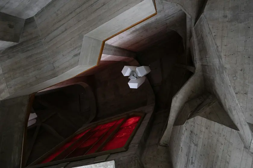 Intérieur d'un bâtiment moderne avec des murs en béton, des formes géométriques et une lumière rouge filtrée.